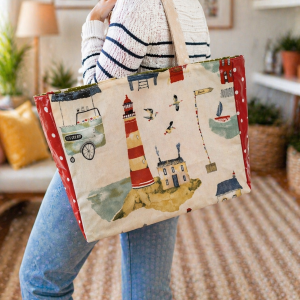 Femme portant à l’épaule un grand sac cabas en coton beige avec motif phare rouge et décor bord de mer